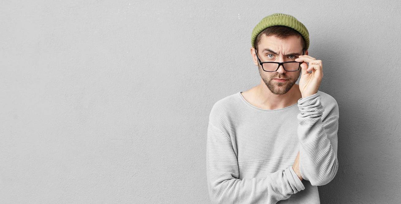 Portrait of serious bearded man looking through glasses, wearing loose sweater and yellow trousers,